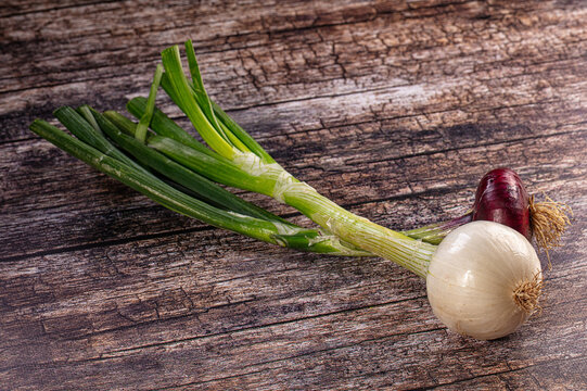 Fresh green spring onions and red onion on rustic wood