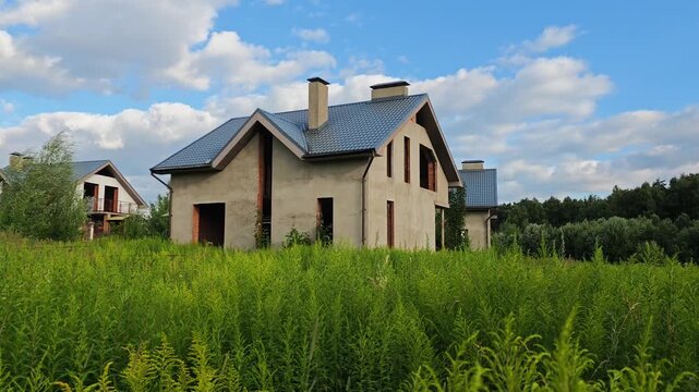 Abandoned unfinished house in a suburban development area with a field of yellow solidago grass swaying in the wind, concept of construction halt, financial real estate crisis and property boundary