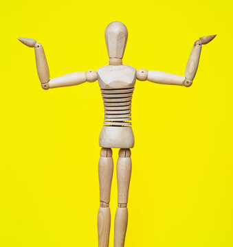 The wooden figure imitates the gesture of an Eastern girl performing a belly dance, spreading her arms and palms outward against a yellow background. A gesture of bewilderment.