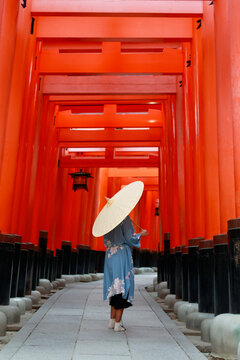 Woman in Blue Kimono Walking with Paper Umbrella Through Red Torii Gate Tunnel at Fushimi Inari Kyoto