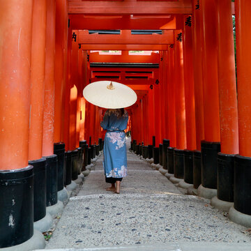 Woman in Blue Kimono Walking with Paper Umbrella Through Red Torii Gate Tunnel at Fushimi Inari Kyoto