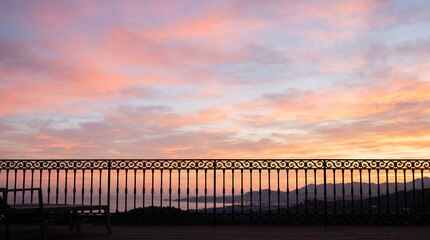 Obraz premium Wrought iron railing silhouetted against a pink and orange coastal sunset