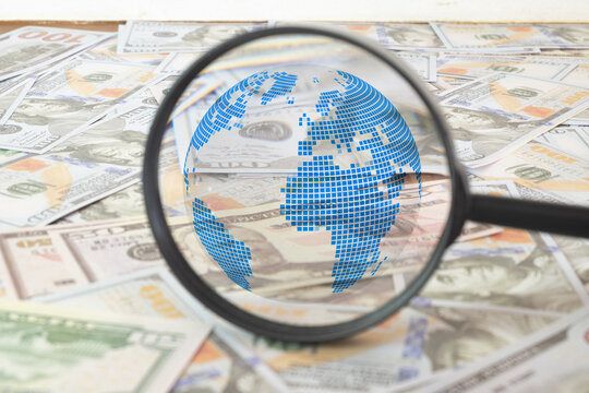 Global economy and international finance concept. Magnifying glass with digital blue earth globe graphic over US dollar banknotes. Worldwide investment, financial research and business.
