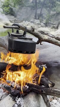 Vertical video of teapots brewing on a wood fire over a rocky canyon river