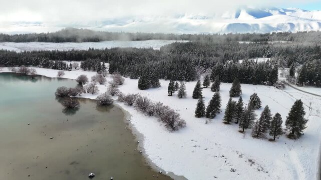 Aerial drone footage of Lake Tekapo during winter, showcasing snow-covered landscapes, turquoise waters, alpine forests, and mountain scenery in New Zealand's South Island.