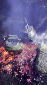 Vertical video of traditional teapots warming on a cozy night campfire