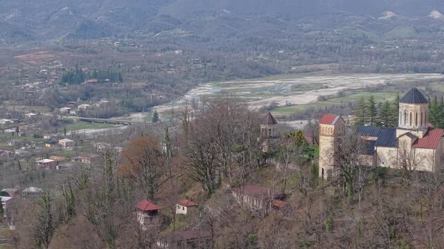 Lateral drone shot revealing Martvili Monastery perched on a hill, with the winding river, lush valley, and scenic landscape of western Georgia stretching into the background.