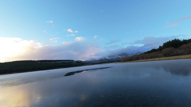 FPV drone captures stunning aerial footage of Laguna La Zeta at sunset in Patagonia, with vibrant sky reflections, pristine lake waters, dramatic mountain views, and tranquil golden hour lighting.
