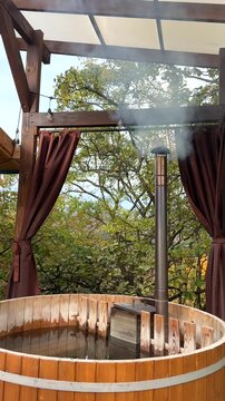 Wooden hot tub emits smoke in a serene outdoor environment surrounded by lush greenery. Relaxation concept.