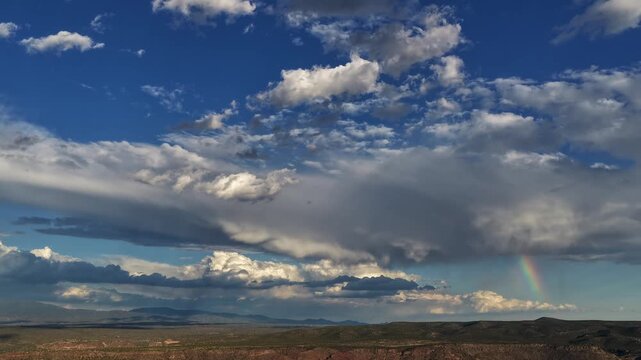 4K drone timelapse capturing a shifting regional climate and dynamic weather. A vibrant segment of a rainbow shines beneath stunning storm clouds over a dark ridge in the four corner states region.