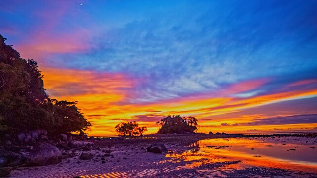 A vibrant time lapse captures colorful clouds drifting across the sky above Ping island at Naiyang Beach Phuket, with glowing orange and purple hues reflecting on calm ocean waters.