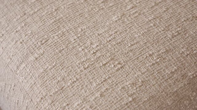 Slow zoom in macro shot highlighting the woven texture and natural detail of a beige linen sofa cushion in warm daylight.