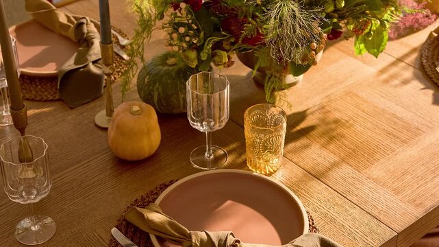 Slow zoom in over a professionally styled rustic wooden dining table featuring plates and glassware bathed in warm natural sunlight.