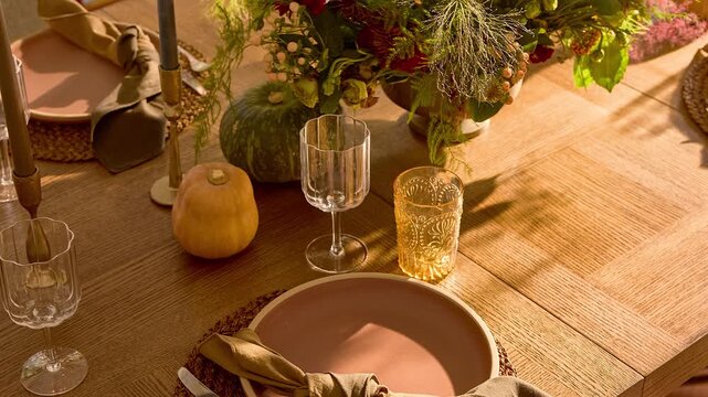 Slow zoom out over a professionally staged rustic wooden dining table with plates and glassware illuminated by warm natural sunlight.