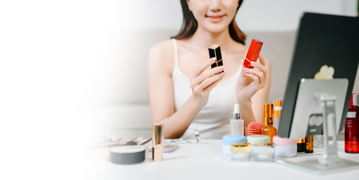  Asian woman carefully applies lipstick in front of a vanity mirror, highlighting her daily beauty and makeup routine.