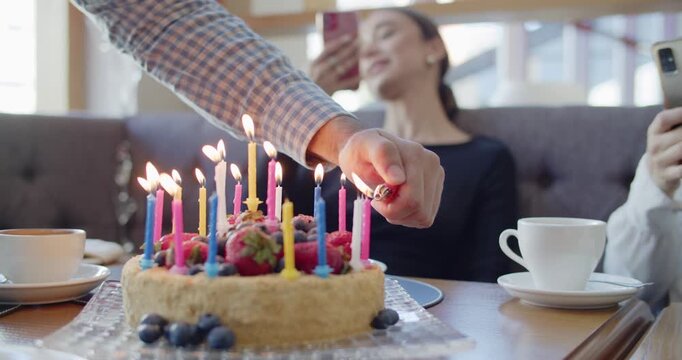 Lighting Colorful Birthday Candles on a Fruit-Topped Cake While Friends Capture the Celebration on Smartphones