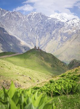 Historical Gergeti trinity church on top of the hill surounded by green nature and mountain in the background. Travelous in KAzbegi national park. Georgia