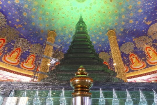 In the emerald green silence of Wat Paknam Phasi Charoen, the glass chedi rises like a glowing heart of light. Golden pillars support a cosmic ceiling that plunges the room into a sense of infinity. The wall paintings tell of Buddha's path to enlightenment and combine earthly beauty with spiritual depth that makes this place so unique, Phasi Charoen district, Thonburi, Bangkok, Thailand