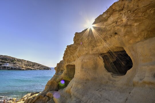 Neolithic caves, former hippie paradise, sun rays break through rocks and illuminate a cave by the sea, Matala, south coast, Crete, Greek Islands, Greece