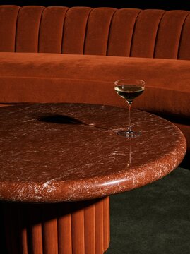 Cocktail glass on a polished brown stone table beside a rust velvet booth
