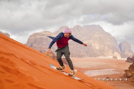 Man successfully sandboarding down steep red dune in Wadi rum showing skill balance confidence achievement and adventure Jordan