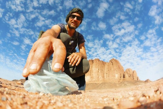 Environmental hiker picks up old plastic bottle waste in Wadi Rum desert, Jordan. A powerful scene highlighting sustainability, conservation, and individual action for Earth Day awareness.Jordan trail