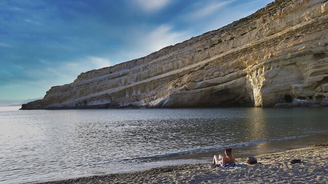 Neolithic caves, former hippie paradise, rocky coast with calm sea and blue sky, two people on the beach, Matala, south coast, Crete, Greek Islands, Greece