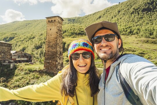 Smiling happy caucasian couple taking selfie by Ushguli svan tower settlement. Hiking in Svaneti Georgia. Man woman backpacking outdoors near historical Unesco world heritage site