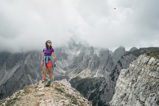 Woman hiker on viewpoint by Dramatic jagged limestone peaks Sesto Dolomites range sharp spires alpine geology viewpoint overview cloudy sky Parco Natural Tre Cime Veneto Belluno Italy summer