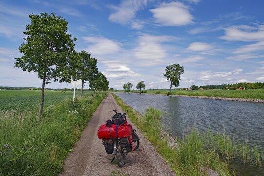 Cycling on a narrow canal path with a landscape of water and trees under a blue sky, bicycle tours, G&ouml;ta Canal, T&ouml;raboda, V&auml;stra G&ouml;talands l&auml;n, Sweden