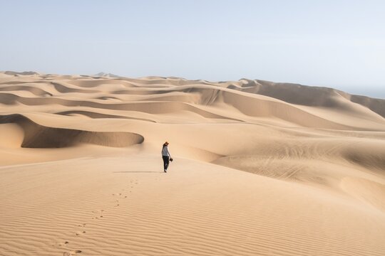 Woman with camera, lonely person walking across dunes, sand dunes with wave pattern, dune sea, sandy desert, impressive desert landscape, Namib Naukluft Park, Namib Desert, Namibia