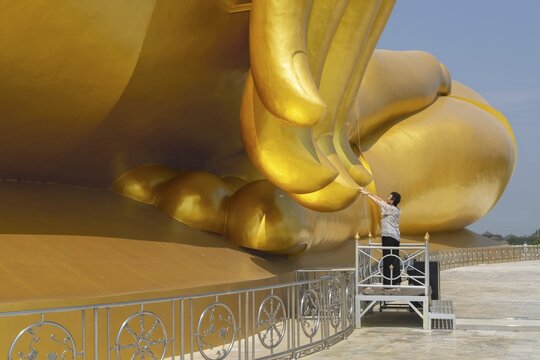 Largest Buddha statue in Thailand (Luang Pho Yai), woman 60-70 touches the fingertips of the statue because according to local belief this brings good luck and success, Wat Muang, Ang Thong, Amphoe Wiset Chai Chan province, Thailand