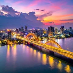 Fototapeta premium Aerial view of a city at sunset with a distinctive illuminated arched bridge over a river, vibrant sky with reflections