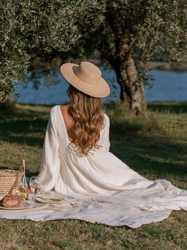 Person in white dress and straw hat at picnic by water
