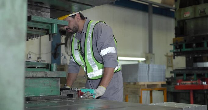 Male factory worker in hard hat and safety vest operating large metal press machine in factory