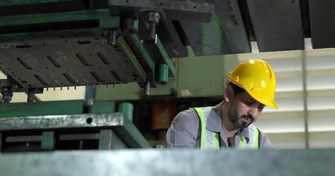 Male factory worker in hard hat and safety vest operating large metal press machine in factory