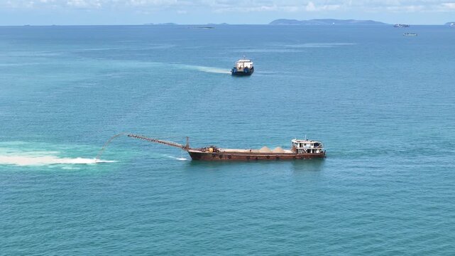 Sand dredging ship discharging sand into the sea for land reclamation project. Coastal engineering and marine infrastructure development. Industrial vessel working on artificial island construction.