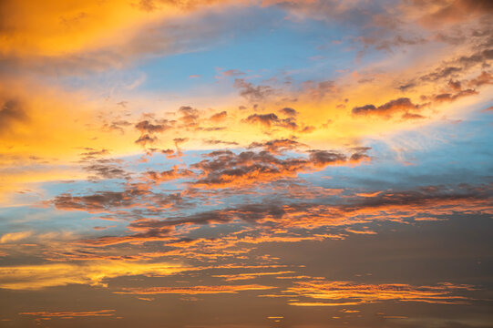 Golden Sunset Cloudscape Background, Fiery Orange and Yellow Atmospheric Clouds Blending into Blue Sky at Dusk.