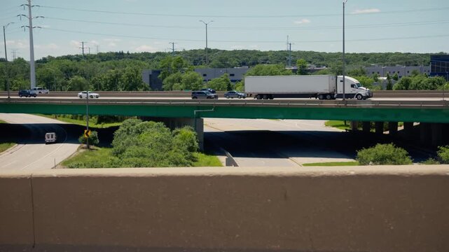 White semi truck transporting freight across an interstate highway overpass on a bright summer day.