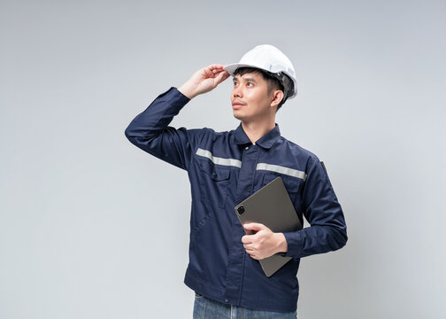 Asian male industrial engineer looking up while holding digital tablet and touching hardhat brim. Concept for visionary technology, mobile banking service, and digital advertising mockup.