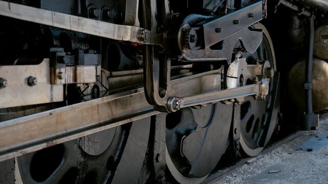 Close up view of the running gear and driving wheels on steam locomotive. Detailed view of the connecting rods, valve gear, wheels, and mechanical components