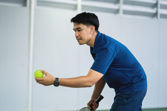 Asian Male Tennis Player Preparing to Serve on Indoor Tennis Court During Professional Training Session Demonstrating Focus, Precision, pirit