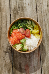 Salmon poke bowl in a delivery box on a wooden surface. Isolated © Cavan