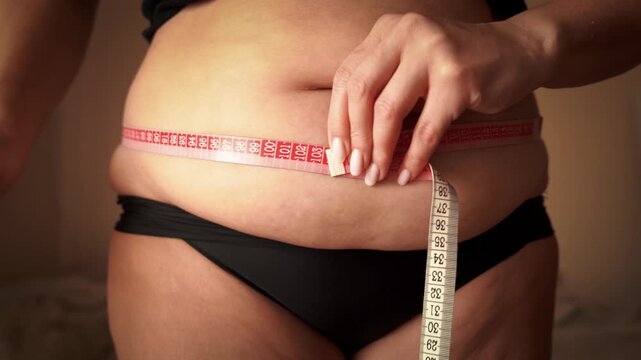 Woman measuring waist with tape measure as weight management concept