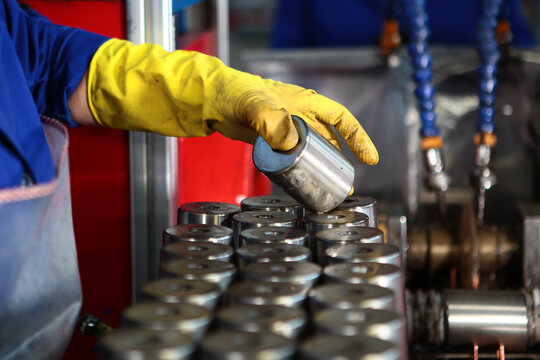 Worker's hand in a yellow protective glove is laying bearings for their subsequent oil treatment. Factory production. Manual labor and quality control. Conveyor belt for the production of bearings