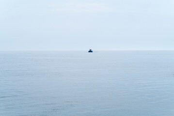 Naklejka premium Small distant boat on calm blue sea The Concept of solitude and vastness