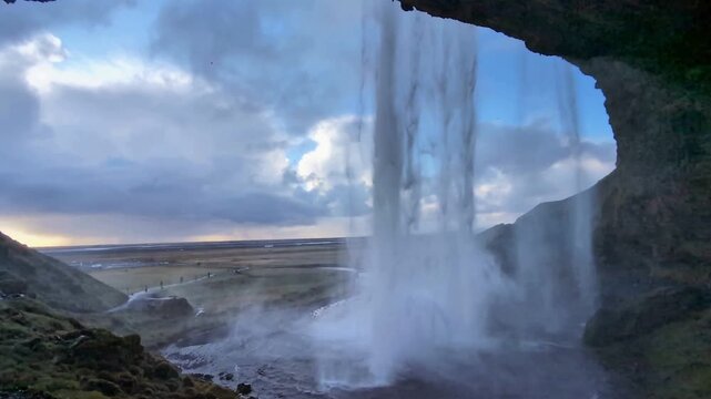 Majestic waterfall view from inside a rocky cave, scenic mountain landscape at sunset, powerful water cascade falling from cliff edge