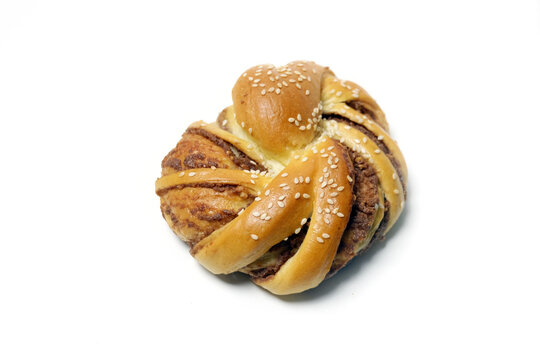 Top view of a golden-brown twisted bread bun filled with sweet paste and topped with sesame seeds on a white background.