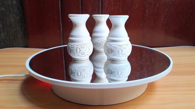 Three miniature white ceramic vases for souvenirs with circular ornaments, placed on a roll of photographic film, are a table decoration or display piece typically made of fired clay. 