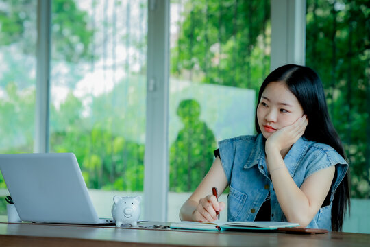 Young Asian woman reading a book with headphones and laptop by the window
